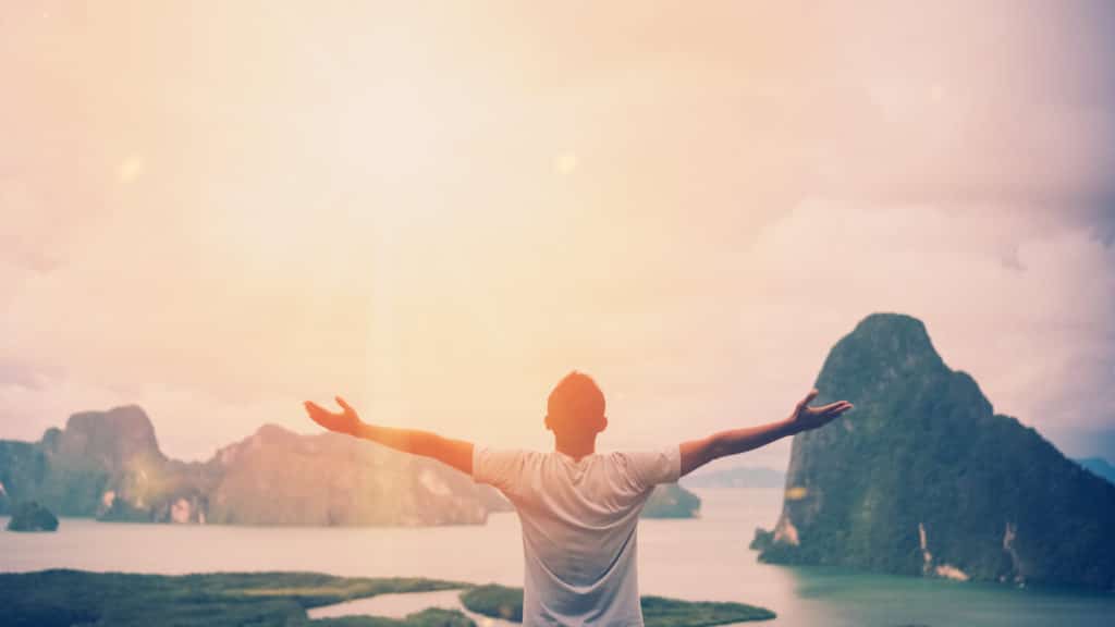 Feel good freedom and travel adventure concept. Copy space of happy man raise hands on top of mountain with sun light abstract background. Vintage tone filter effect color style.