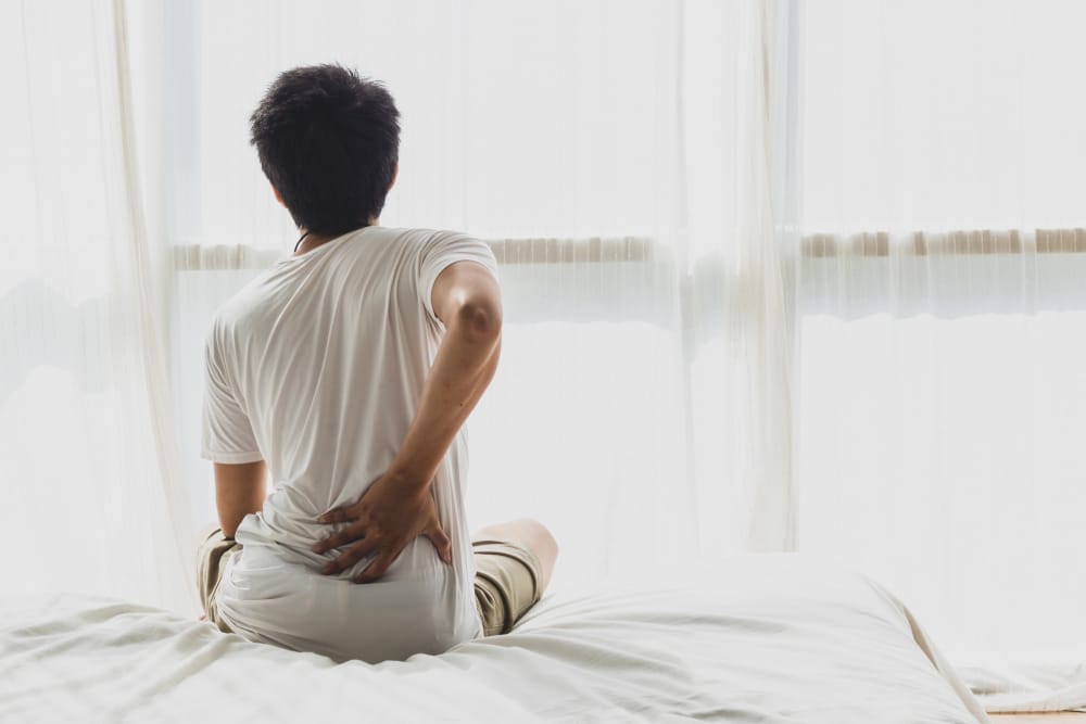 Asian man back pain and sit on bed in bedroom in the morning