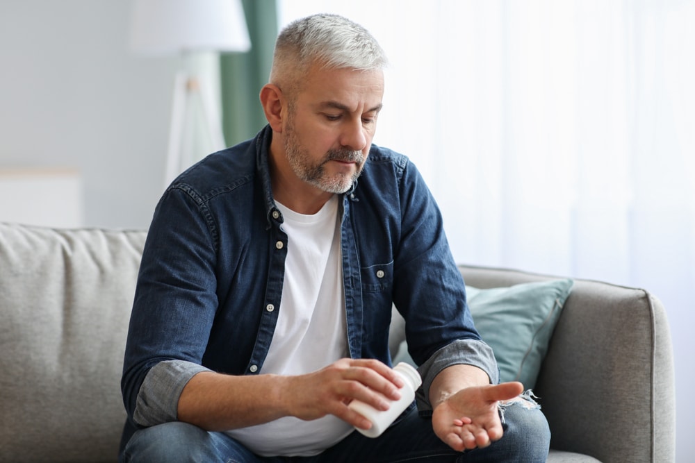 Senior man taking pills while sitting on couch at home