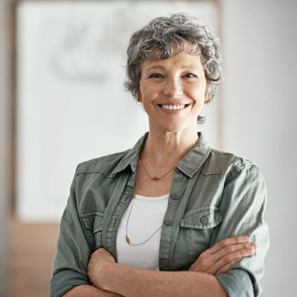 mature woman smiling while standing with her arms folded in her home