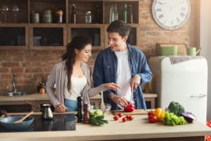 Happy couple cooking dinner together in their loft kitchen at home. Man preparing vegetable salad for his girlfriend, copy space