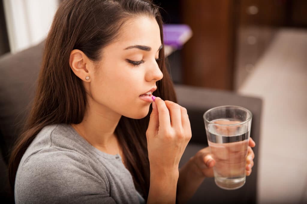 Brunette woman taking a vitamin with a glass of water at home