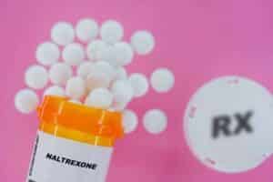 Pills spilling from yellow container on pink background