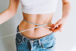 woman measuring her waist's size with tape measure on white background
