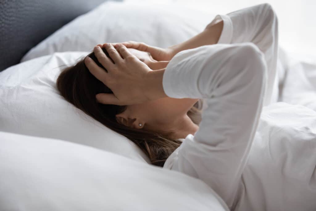 Woman in bed with hands over her face, waking up exhausted after poor sleep due to hormonal imbalance and menopause
