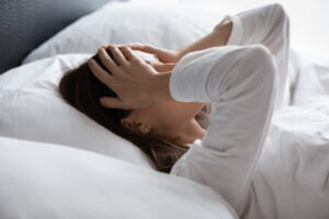 Woman in bed with hands over her face, waking up exhausted after poor sleep due to hormonal imbalance and menopause