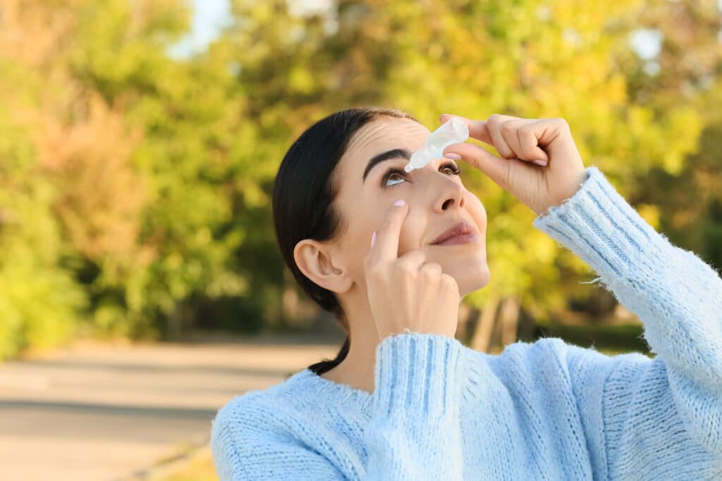 Woman putting in eyedrops outdoors while experiencing seasonal allergies made worse by hormones