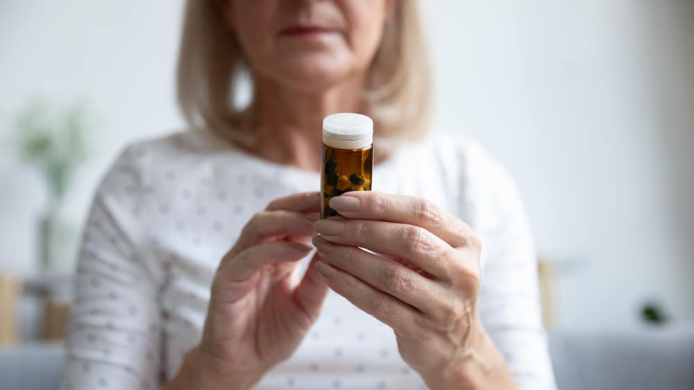 Older woman holding up a bottle of sleeping pills.