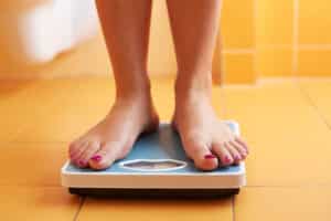 Woman stepping on scale during weight loss plateau that may be due to hormones.