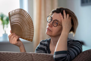 Woman fanning herself during menopausal hot flash.