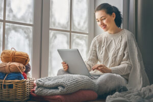 Woman sitting and working on laptop in cozy sweater in the winter time