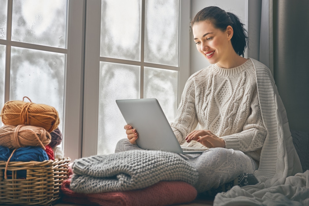 Woman sitting and working on laptop in cozy sweater in the winter time