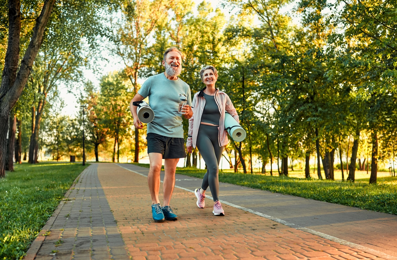 Full length image of beautiful sporty healthy active cheerful middle age couple going to exercise outdoors in park holding mats for yoga, pilates, gym. Sports healthy lifestyle. Loving older couple.