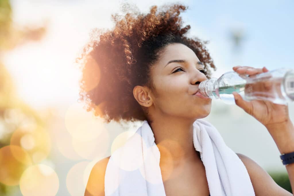 Woman drinking water after exercise, illustrating the importance of hydration for endocrine function & overall wellness.