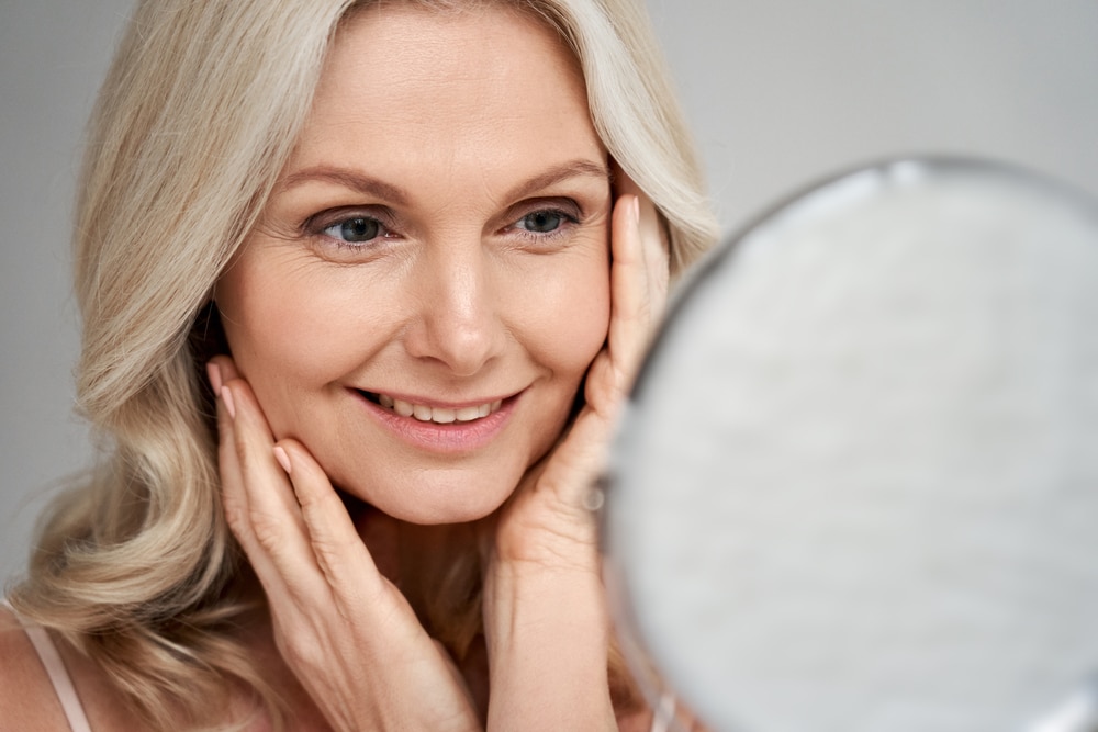Woman looking in a mirror, representing healthier-looking skin and improved skin texture associated with hormone balance and collagen support