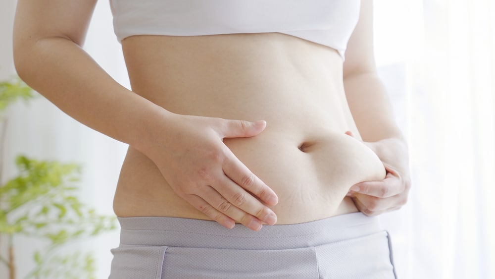 Person holding midsection, representing metabolism changes, weight shifts, and hormone-related body composition concerns.