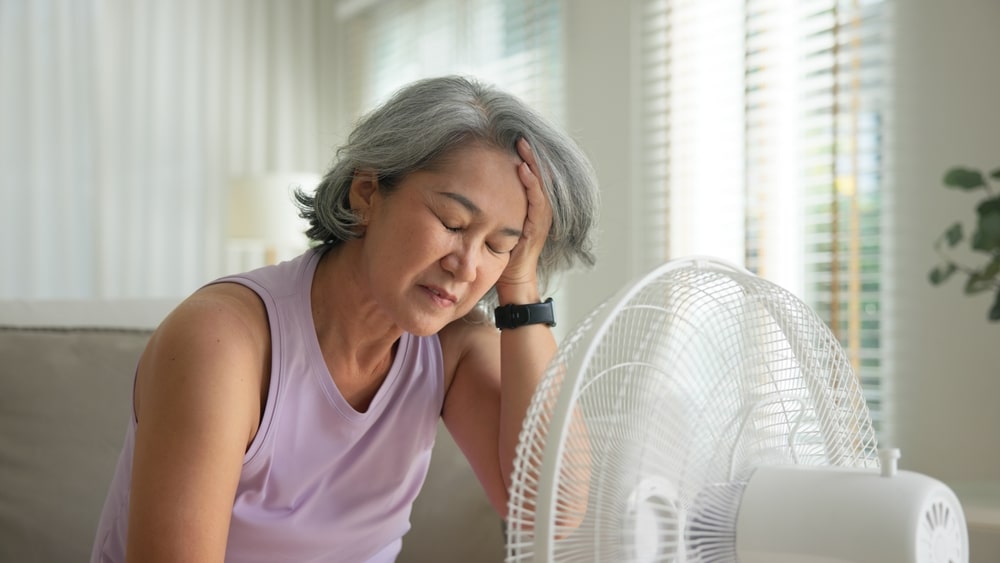 Woman cooling herself with a fan during a hormone-related hot flash or heat sensitivity episode.